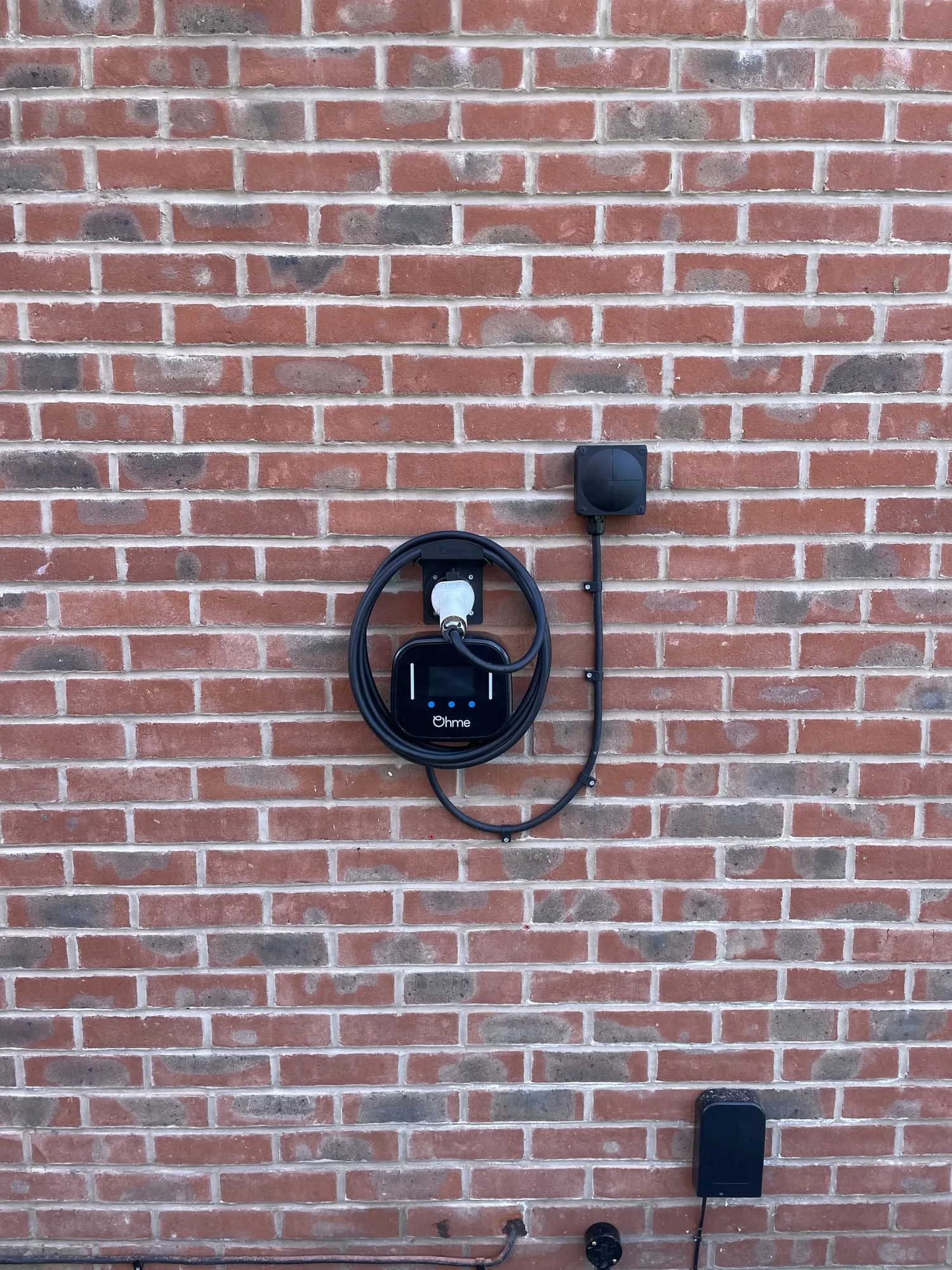 Ohme EV charger installed on a red brick house wall
